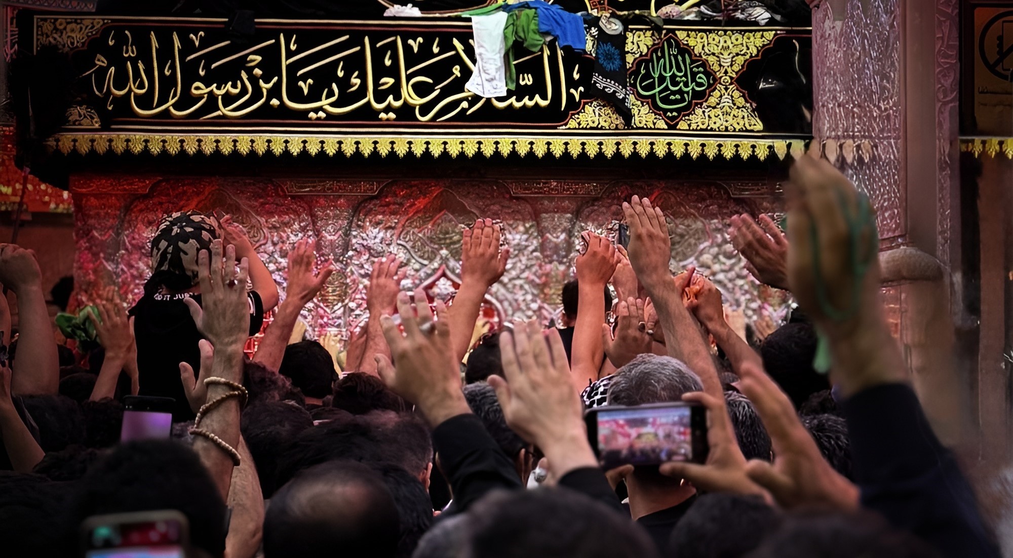 تصویری از آستانه صحن جامع و بخشی از ضریح امام حسین که خیل زائران را در حال ورود به صحن نشان می دهد.